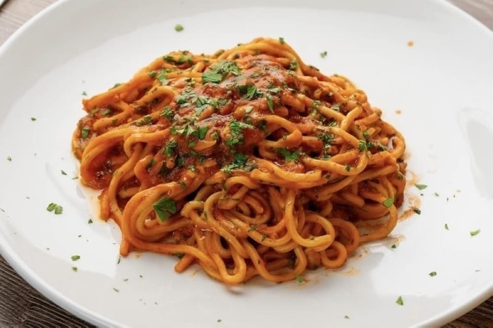 A pasta dish featuring red sauce and topped with green spice flakes. 