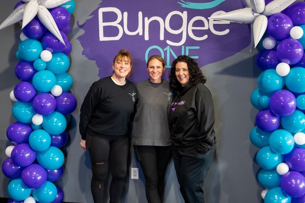 Three women pose in front of BungeeONE sign. 