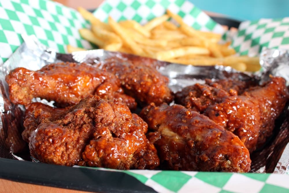 A paper-lined plastic basket filled with fried wings and fries. 