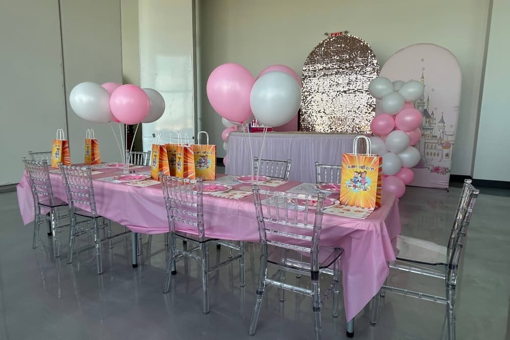 Room set up for a children's party featuring short chairs, pink and white party decorations. 