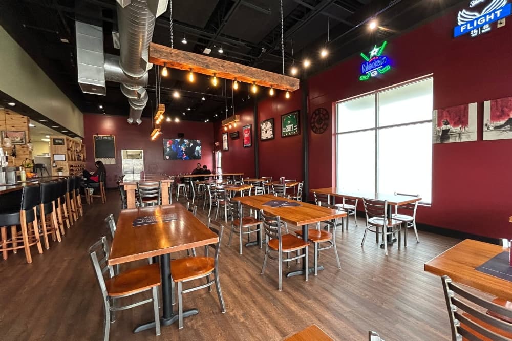 Interior of a restaurant featuring dark red, wood and metal design elements. 