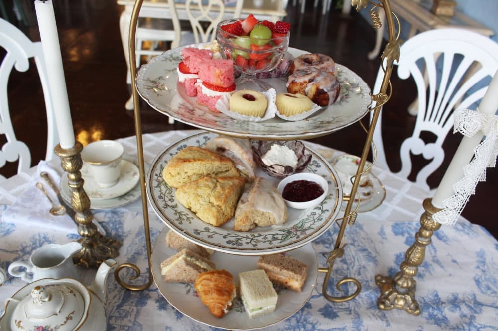Overview of a three-tiered serving dish featuring sandwiches, pastries, fruit and more on plates. 
