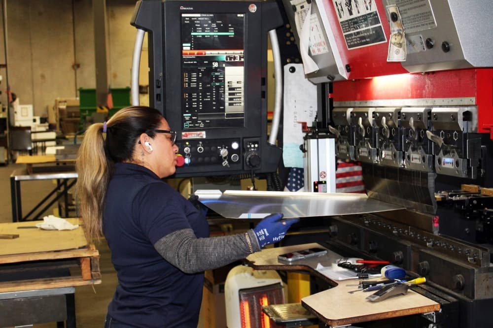 Female feeding a sheet of metal into a cutting machine. 