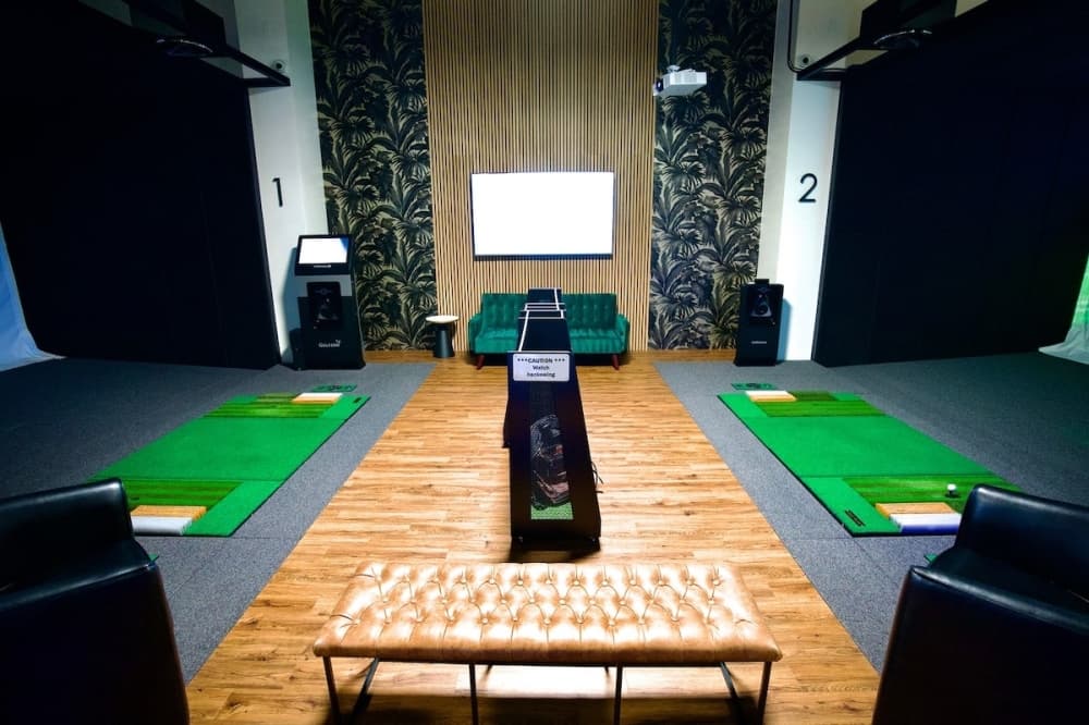 the interior of a golf simulation bay with pleather couches and light hardwood floors