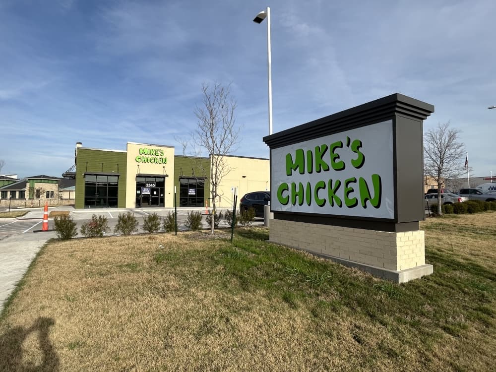 Exterior of a freestanding building and a monument sign, both feature Mike's Chicken signage 