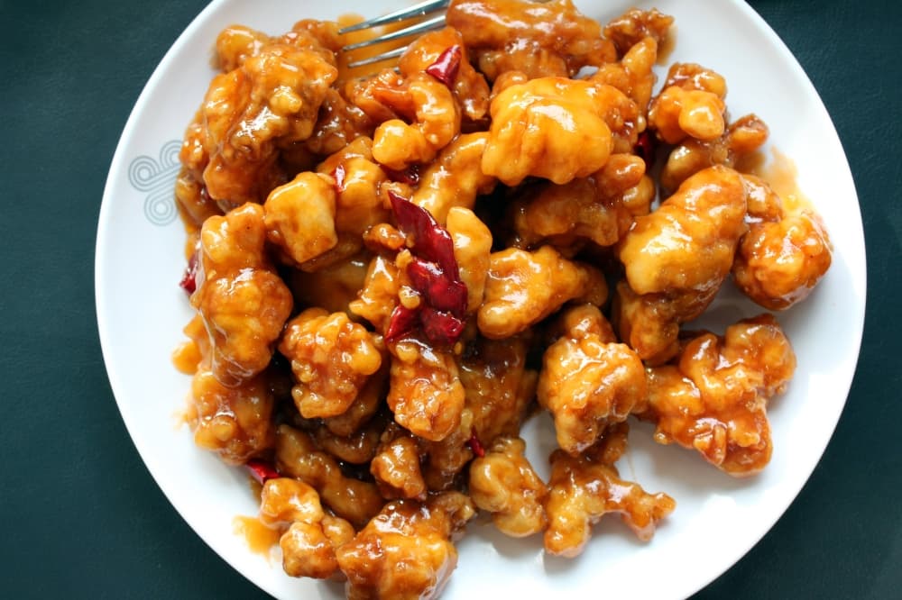 Overview of fried chicken bites covered in an orange sauce on a dish. 