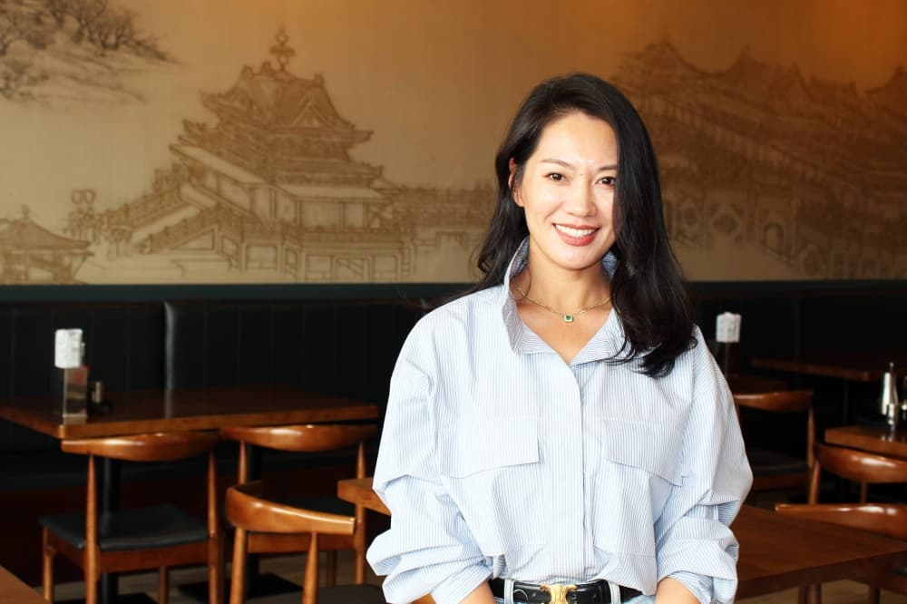 Female standing in a restaurant featuring Chinese architecture wallpaper on the wall behind her. 
