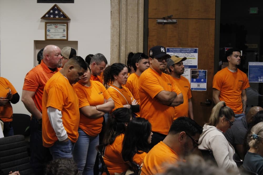 Labor union members stand in the San Marcos council chambers wearing bright orange shirts.