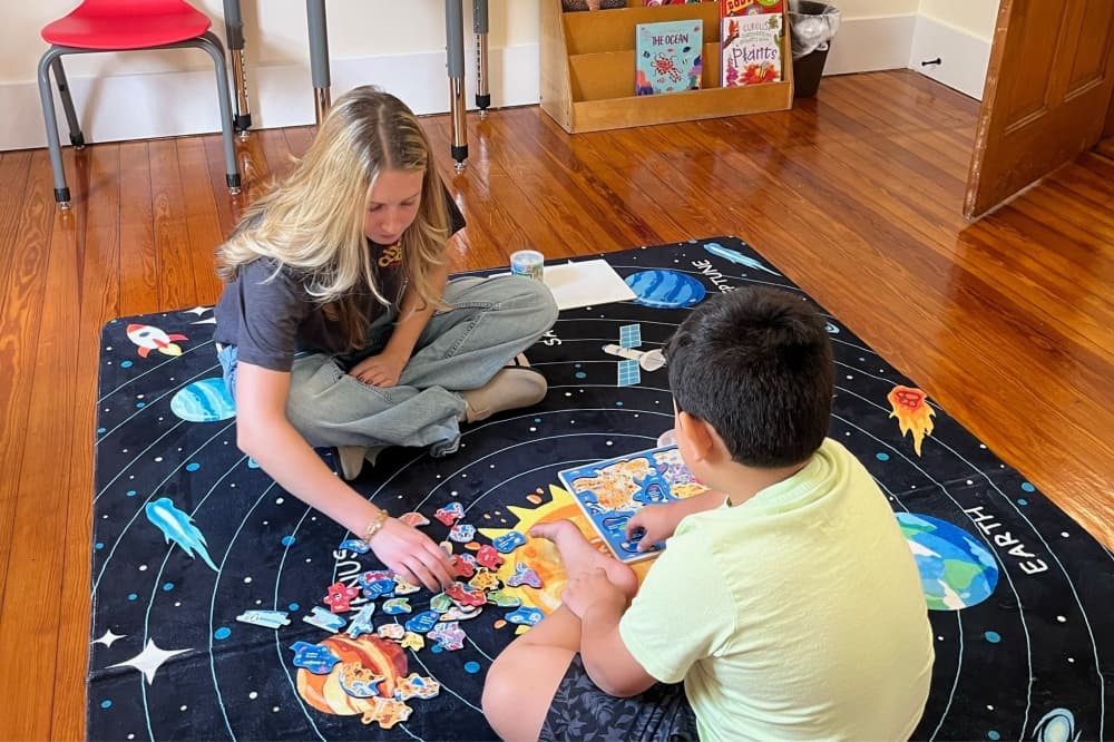 An image of a student aide and child working on a puzzle together. 