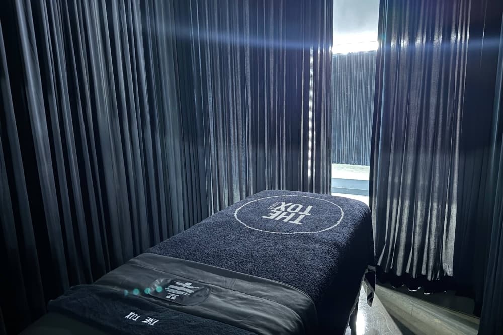 Spa table in a room lined with dark gray curtains. The Tox branding is on the dark gray cushioned table. 