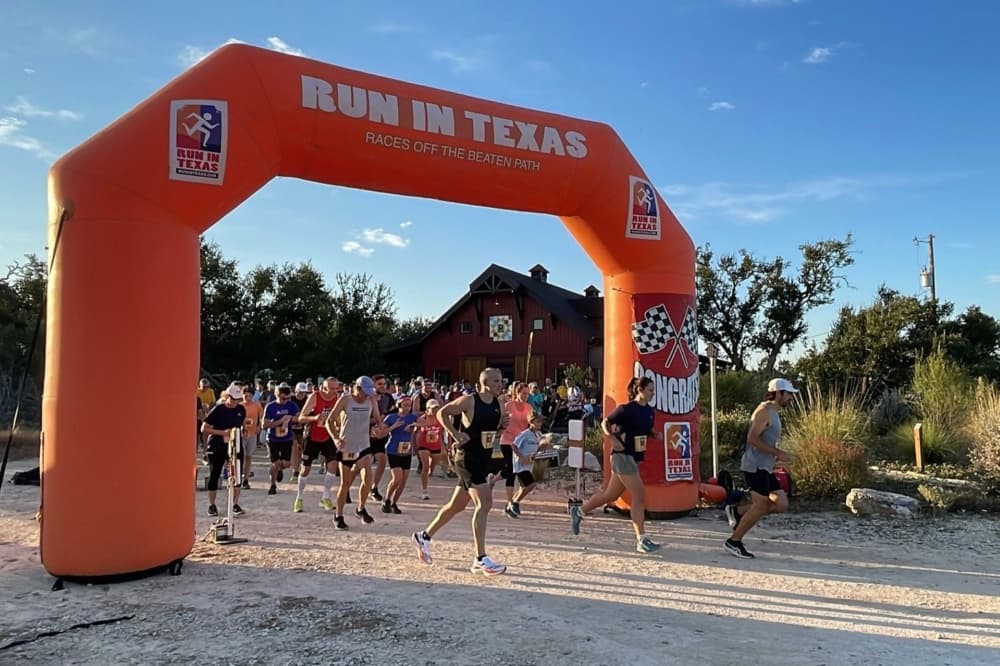A giant orange start-line inflatable is shown with people racing through it.
