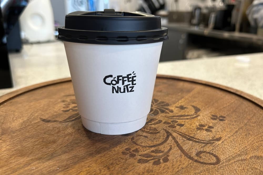 White paper cup with black lid featuring Coffee Nutz branding. 