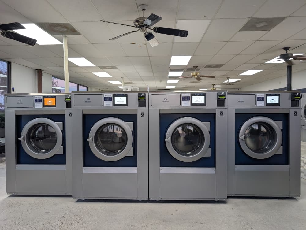 Customers using advanced touchscreen washers and dryers at Royal Hill Laundry in Jersey Village TX, a modern Houston-area laundromat offering self-service laundry, wash and fold, and pickup and delivery options.