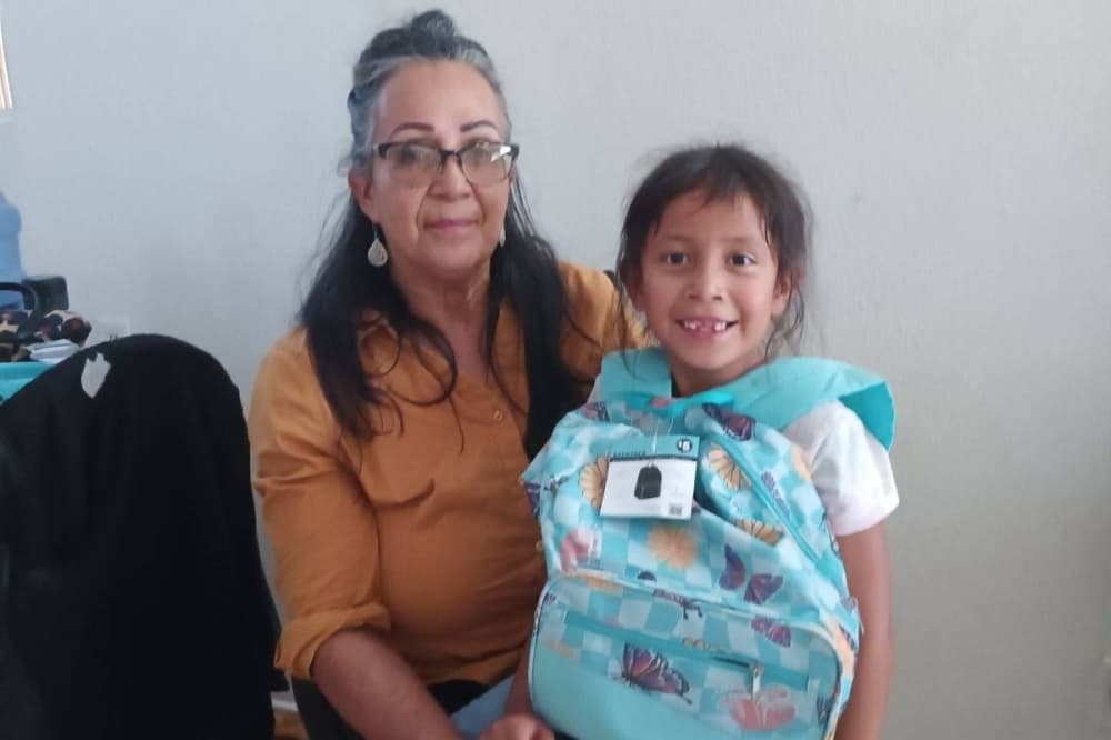 An adult female is seated with a female child in her lap. The girl has a backpack on. 