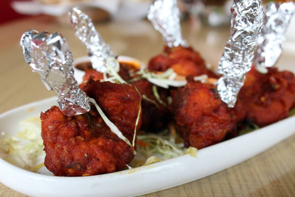 Pieces of chicken coated in a dark red dry rub with aluminum foil over the chicken bones. 
