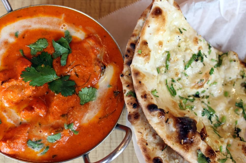 Overview of a red sauce dish in a bowl next to a piece of naan. 