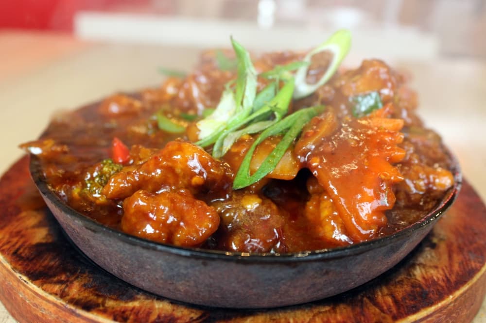 Sideview of chicken in a brown sauce on a metal dish with steam rising from the food. 