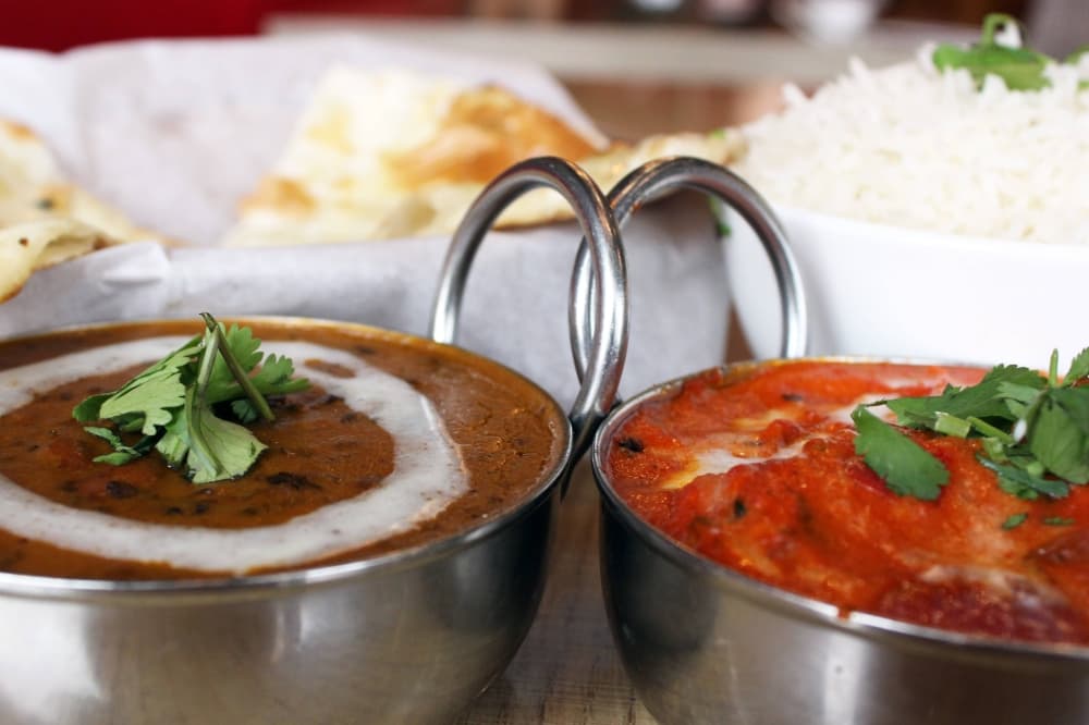 Two dips in separate bowls with bread and rice in dishes in the background. 