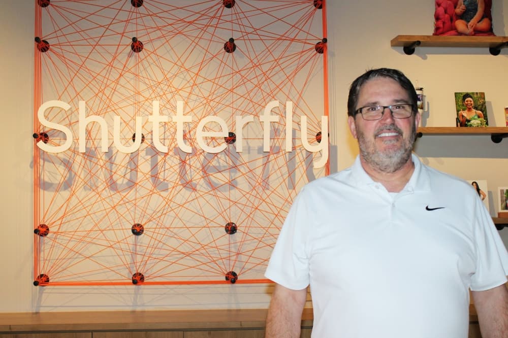 Male standing in front of a wall featuring string art and Shutterfly branding. 