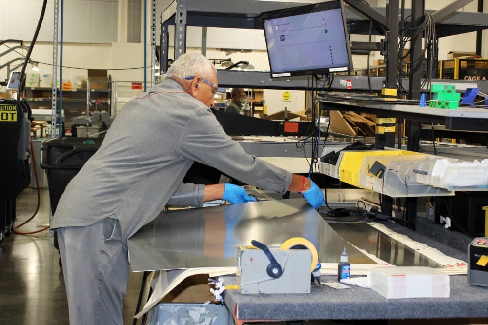 Male working with sheets of metal on a workbench in a manufacturing facility. 
