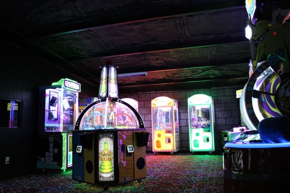 A dark yet colorful arcade room with several claw machines. 