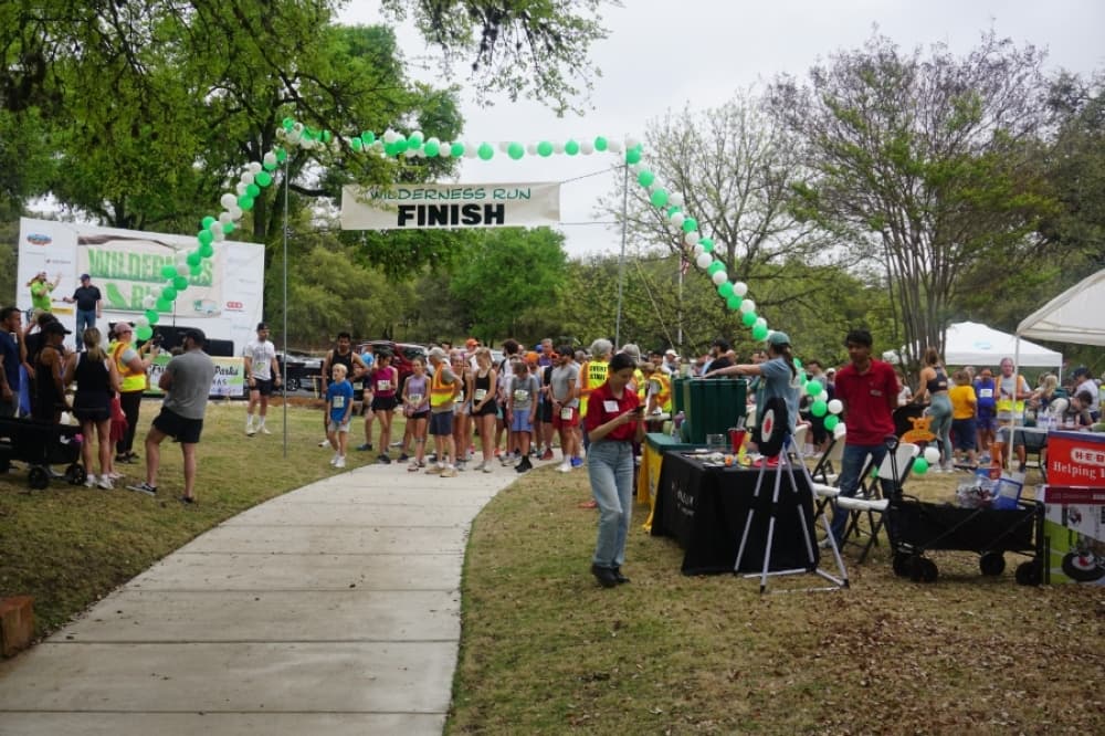 This image shows participants of the 2025 Wilderness Run 5K standing around the finish line at Hurst Creek Sculpture Garden.