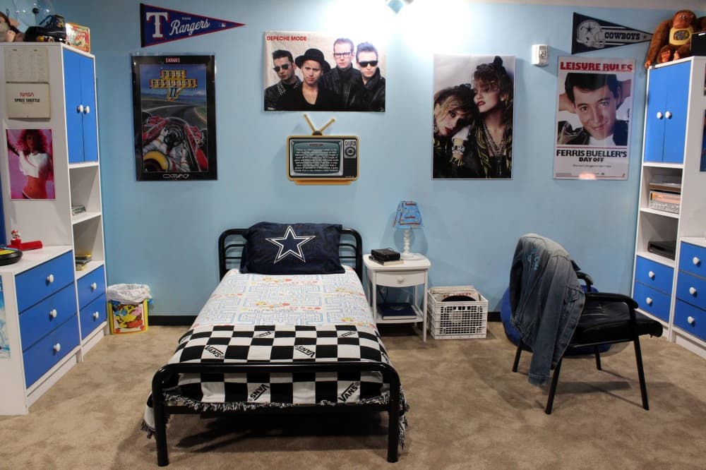 A bedroom scene featuring blue and white decor elements and 80s themed pop culture posters. 
