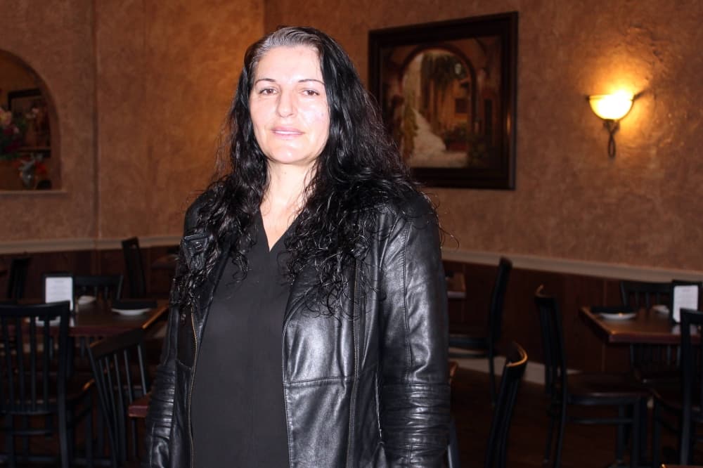 Female wearing a black leather jacket over a black top stands in a dimly lit restaurant. 