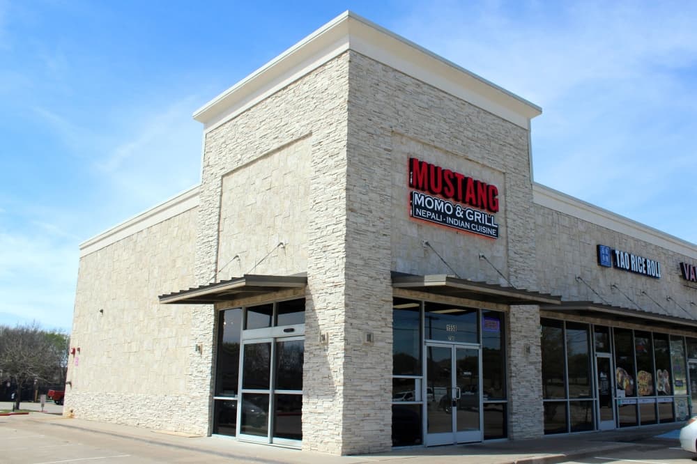 Exterior of a corner space in a strip center featuring Mustang Momo & Grill signage. 