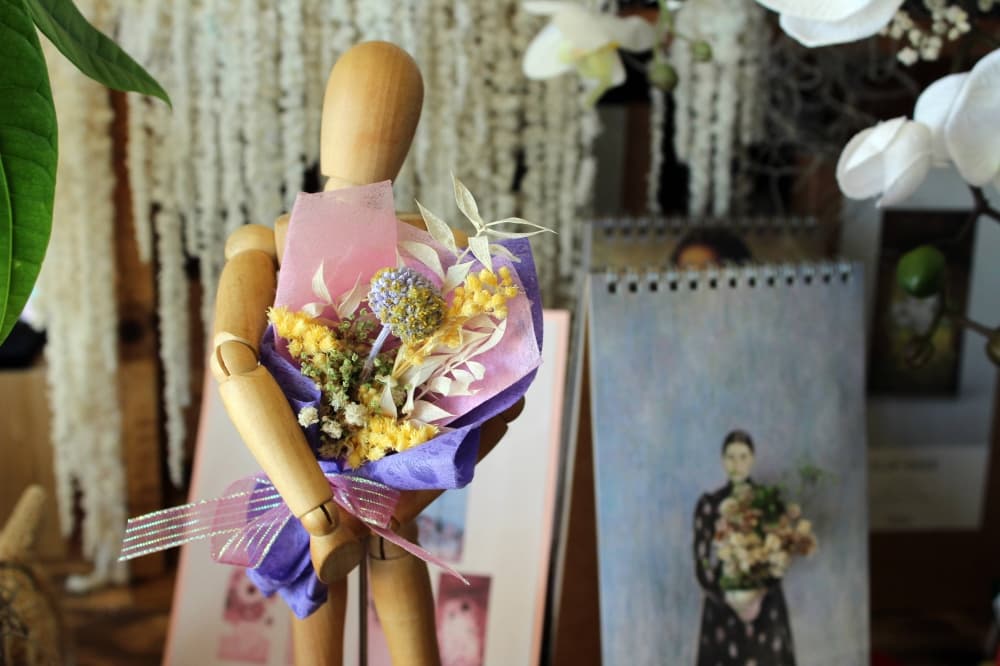 Wooden art mannequin holding a bouquet of dried flowers. 