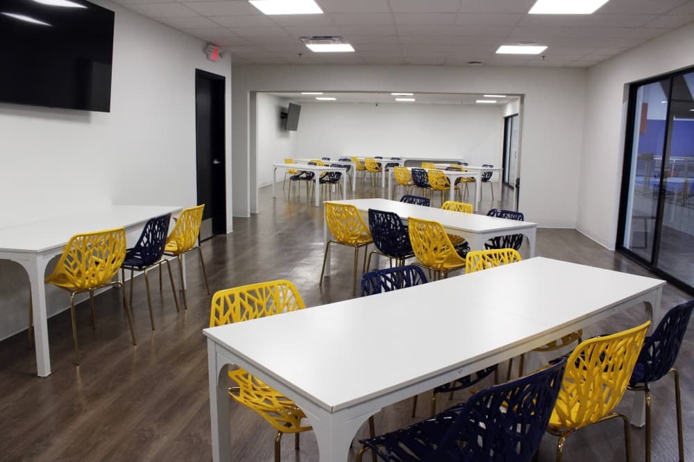 White tables surrounded by dark blue and yellow chairs in a room 