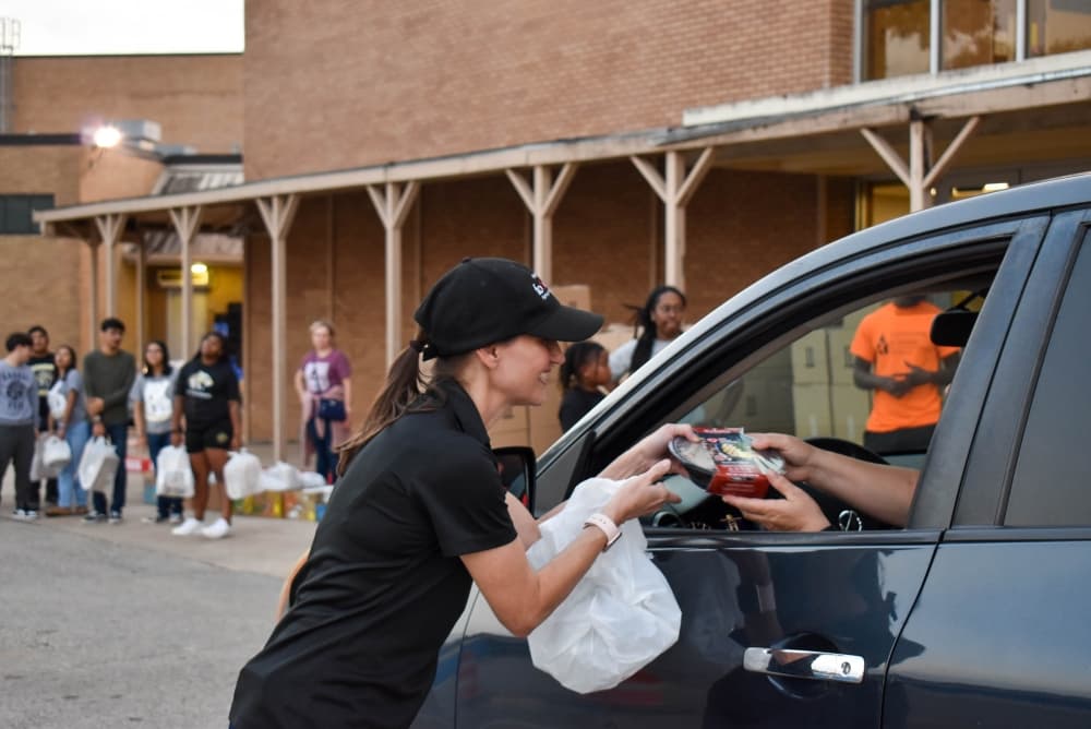 woman hands food through car window.