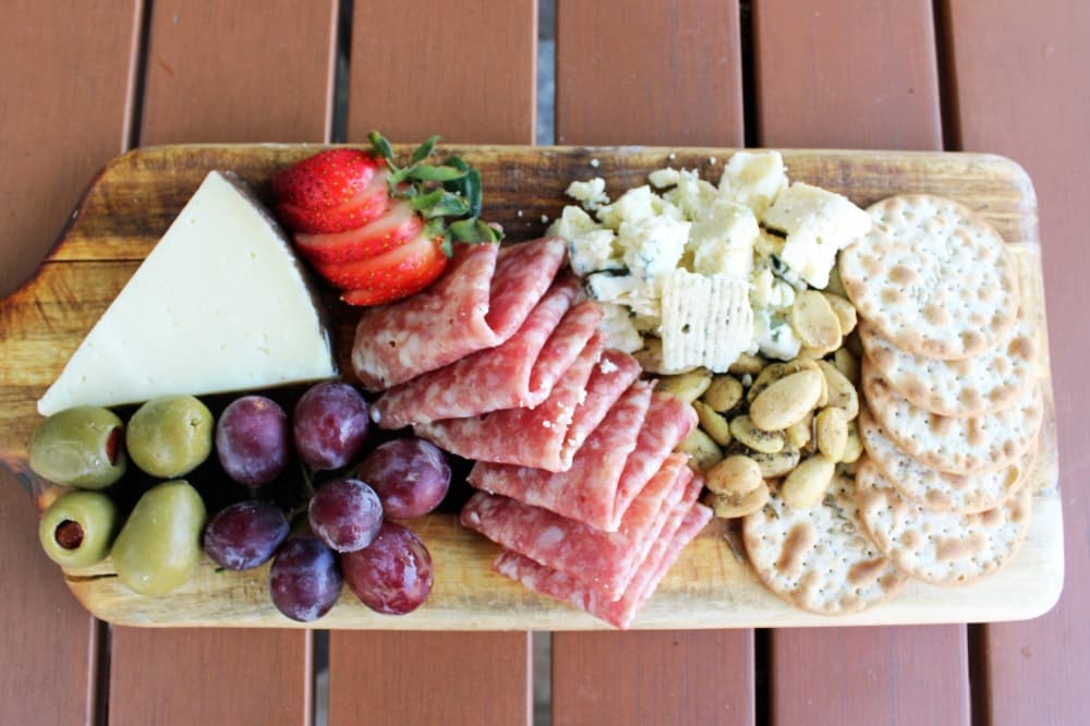 Overview of a meat and cheese board which also includes grapes, strawberries, olives, nuts and crackers.