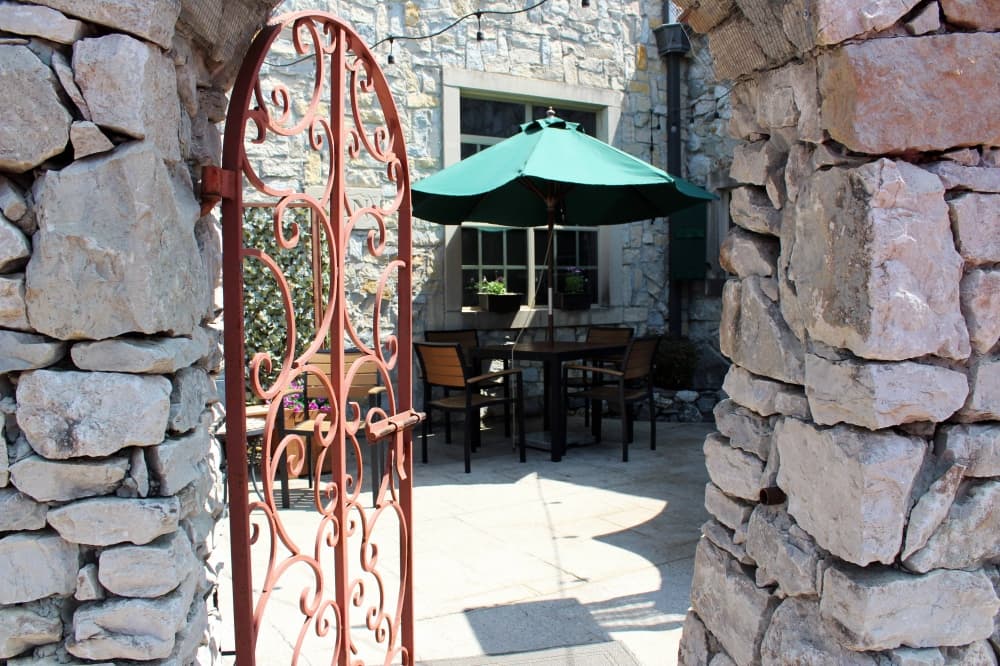 Stone wall featuring a wrought iron gate leading into a restaurant patio. 
