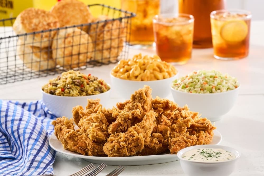 Fried chicken, side dishes, biscuits and glasses of tea on a table.  