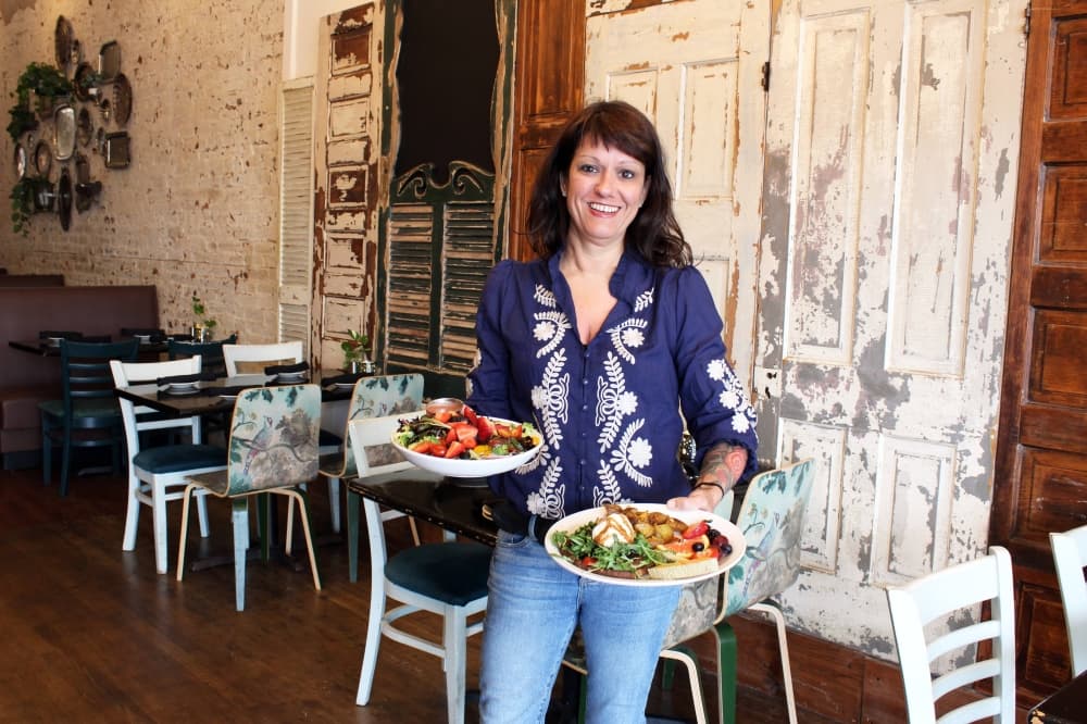 Female holding two plates of food in a bistro featuring rustic wood decor elements. 