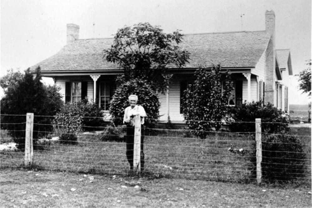 Andrew Pickle, original owner of the Pickle-Mason House, stands in front of his house in a black and white photograph.