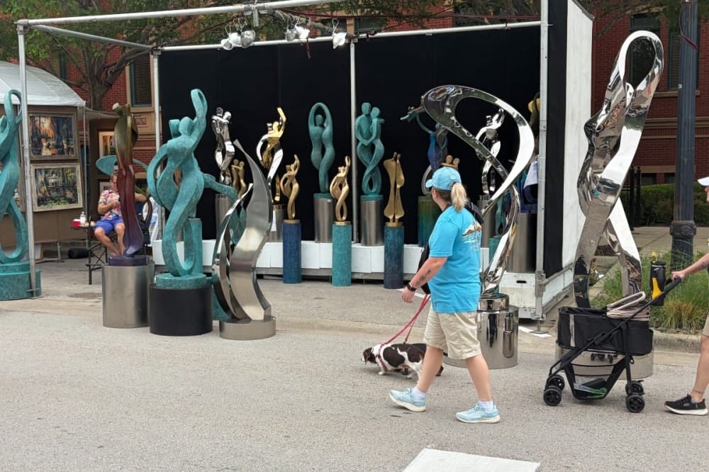 People and dogs walking by a sculpture 
