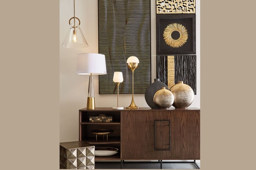 Wood sideboard decorated with two modern gold table lamps and contemporary abstract art.