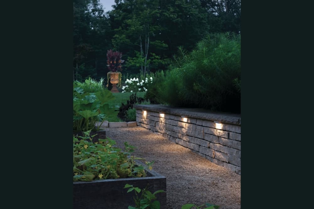 Low-profile stone wall lighting illuminating a garden path and lush landscaping at night.