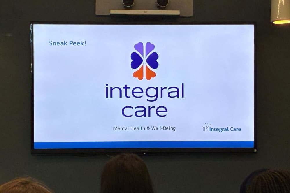 A powerpoint slide on a TV, showing Integral Care's now logo,  a purple brain made up of hearts?