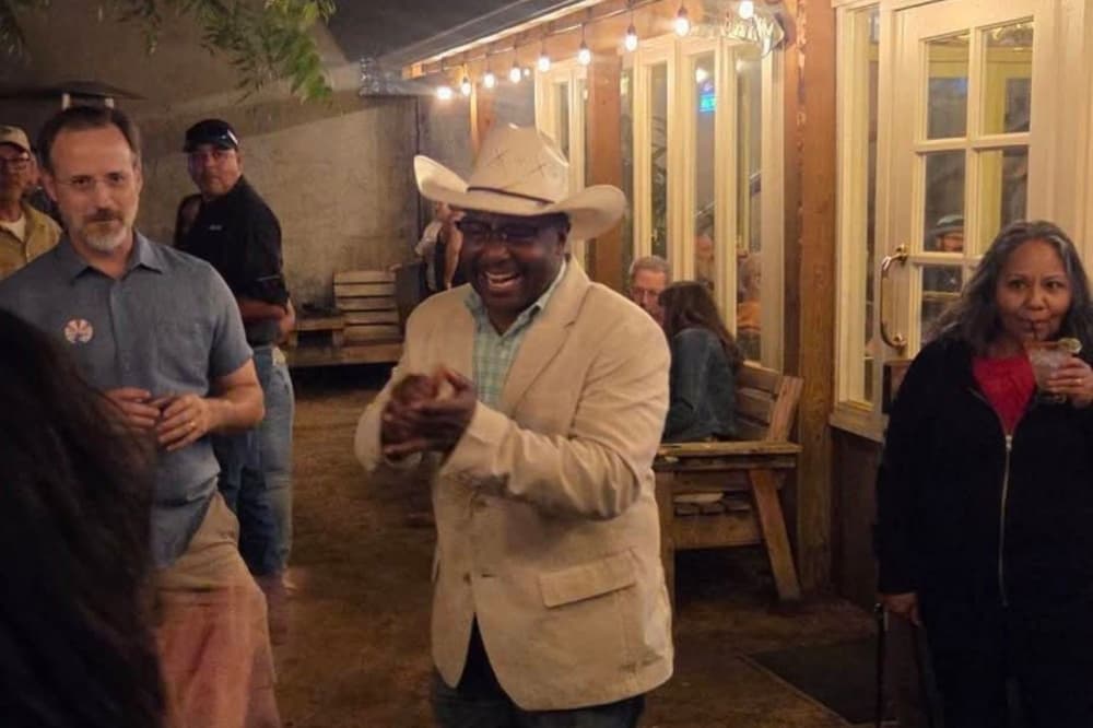 Wearing a matching beige cowboy hat and suite coat, the mayor smiles and claps.