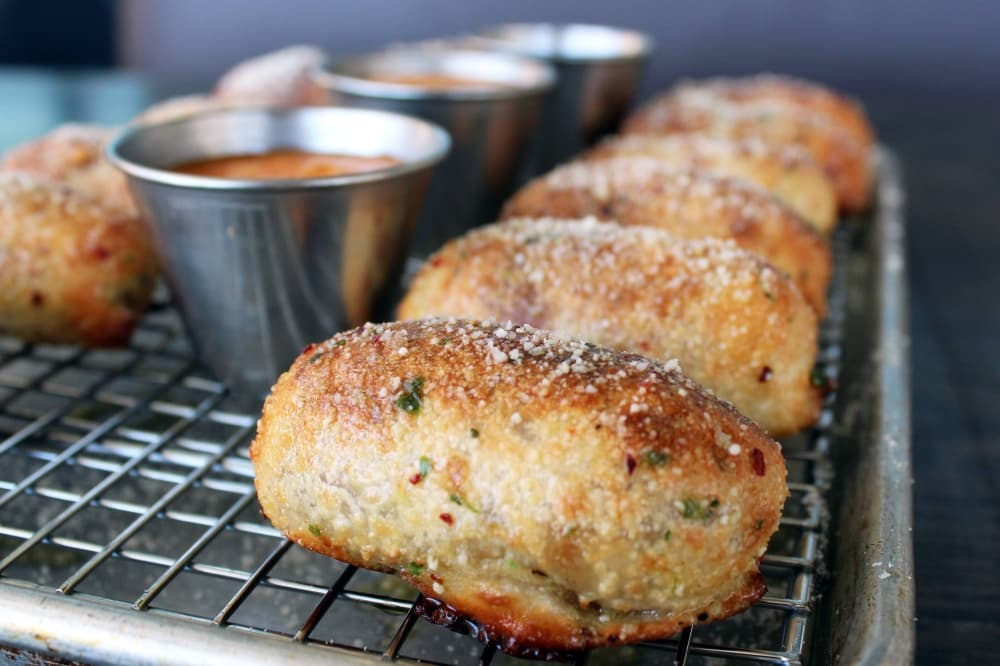 Baked dough items, which are oblong shaped, are dusted with spices and cheese sitting a metal dish. 