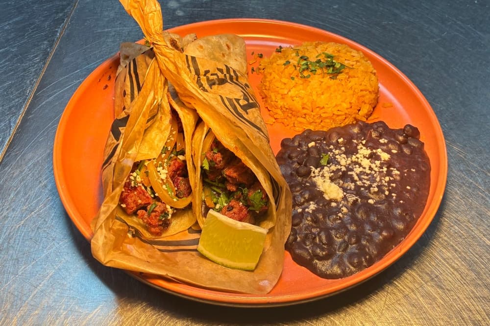 The Pirata Tacos plate ($17) includes two flour tortillas with locally sourced beef fajita, rice and refried black beans, grilled jack cheese, onion and cilantro. The menu blends Mexican-inspired dishes with American comfort food, which rotates seasonally. (Jessica McLaren/Community Impact)