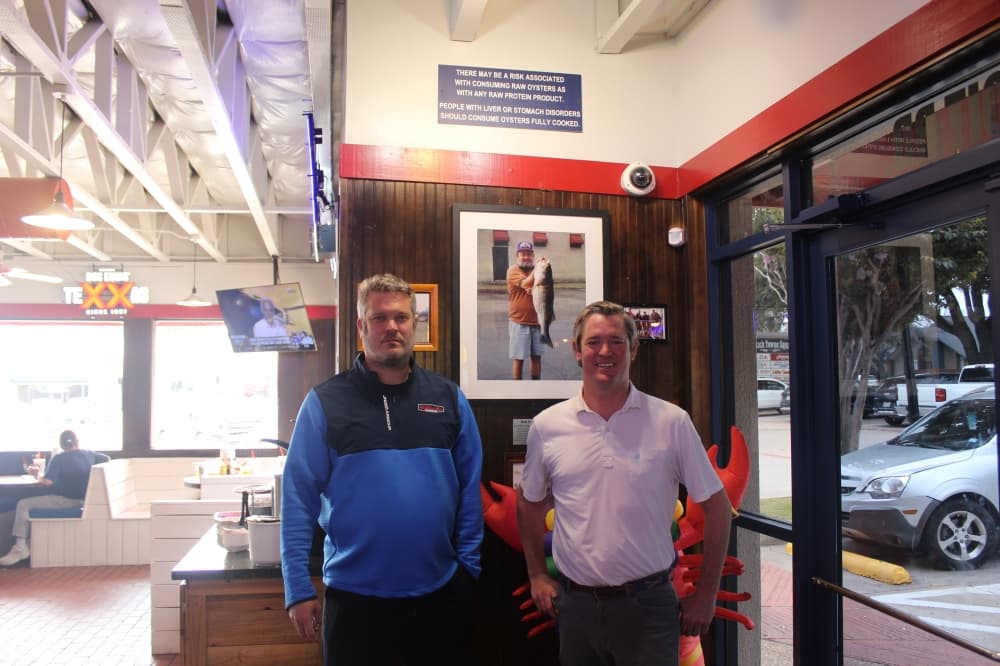 From left, Aw Shucks owners Eric and Nick Peterson stand with a photograph of their father, Bob Peterson. (Michael Crouchley/Community Impact)