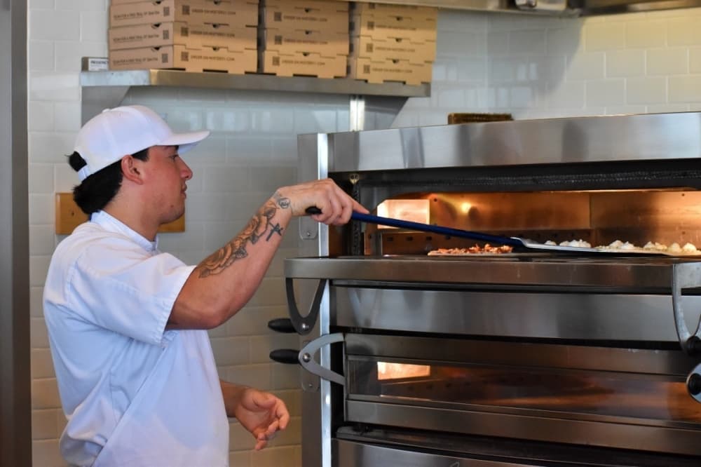 Employee pushing pizza into oven 