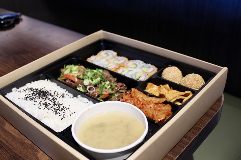 The to-go bento box ($23.95) is made with sushi rolls, ginger and wasabi, bulgogi or spicy pork, white or fried rice, miso soup, cooked kimchi, a side dish and sesame balls. (Jovanna Aguilar/Community Impact)
