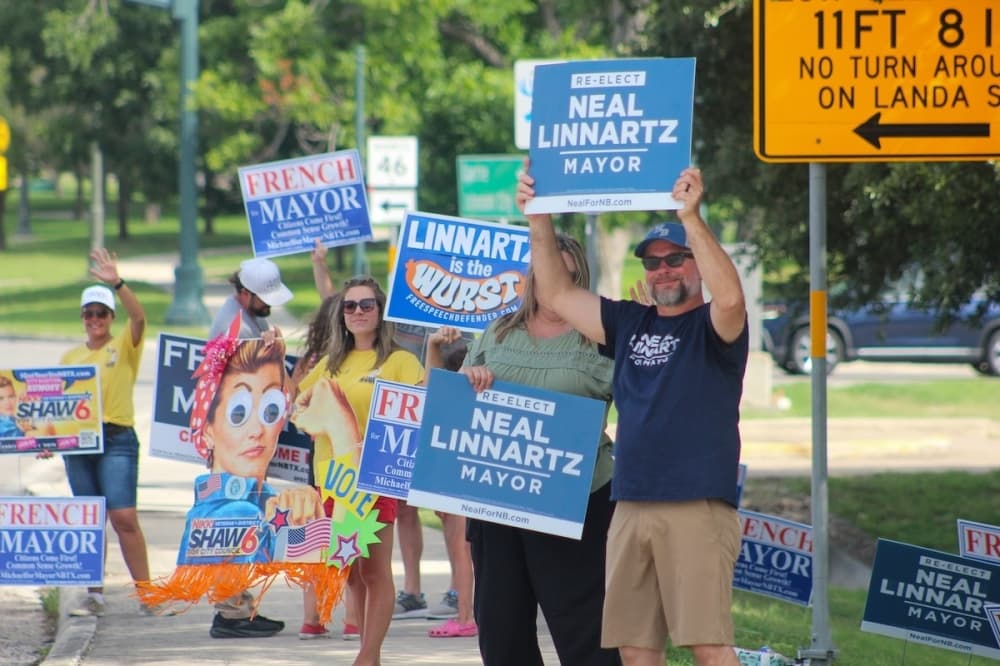 New Braunfels residents hold campaign signs for Incumbent New Braunfels Mayor Neal Linnartz, mayoral candidate Michael French and District 6 candidate Nikki Shaw on June 13 at New Braunfels City Hall. (Amira Van Leeuwen/Community Impact)