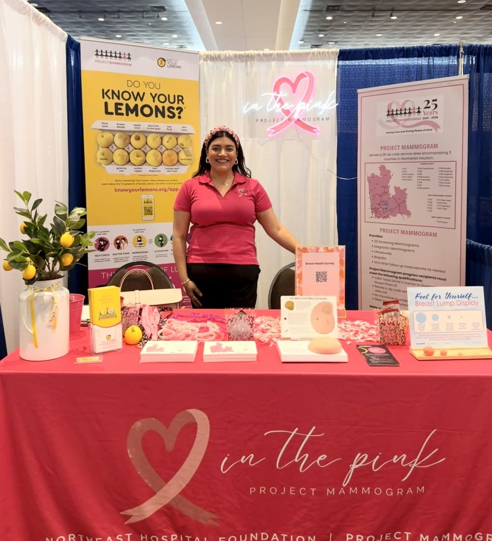 Project Mammogram Coordinator Silvia Torres standing in a pink "Project Mammogram" booth with educational pamphlets in front of her