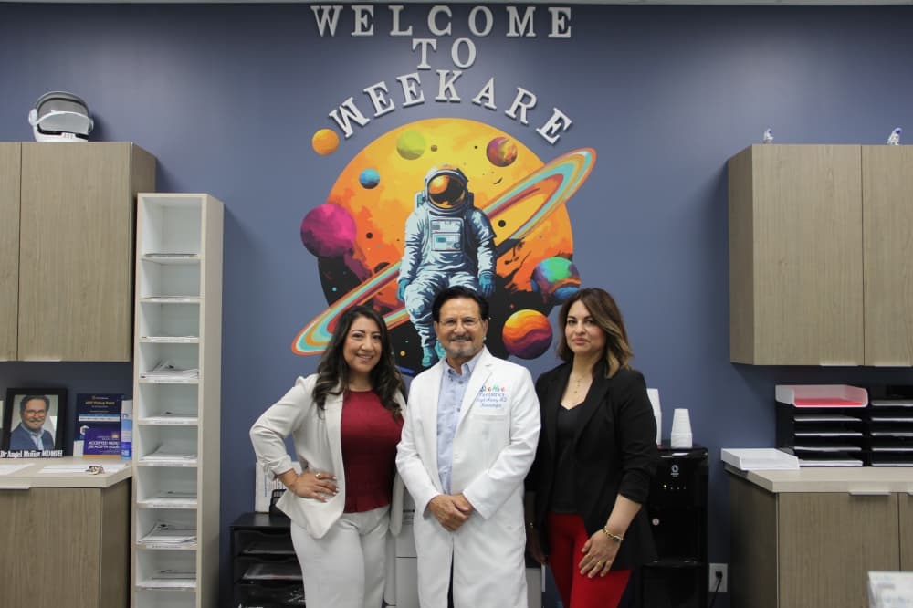 From left, WeeKare Pediatrics Chief Operating Officer Melisa Hernandez, founder Angel Muñoz and Assistant Office Manager Edith Mendez stand in front of the business' logo in the New Caney location. (Wesley Gardner/Community Impact)